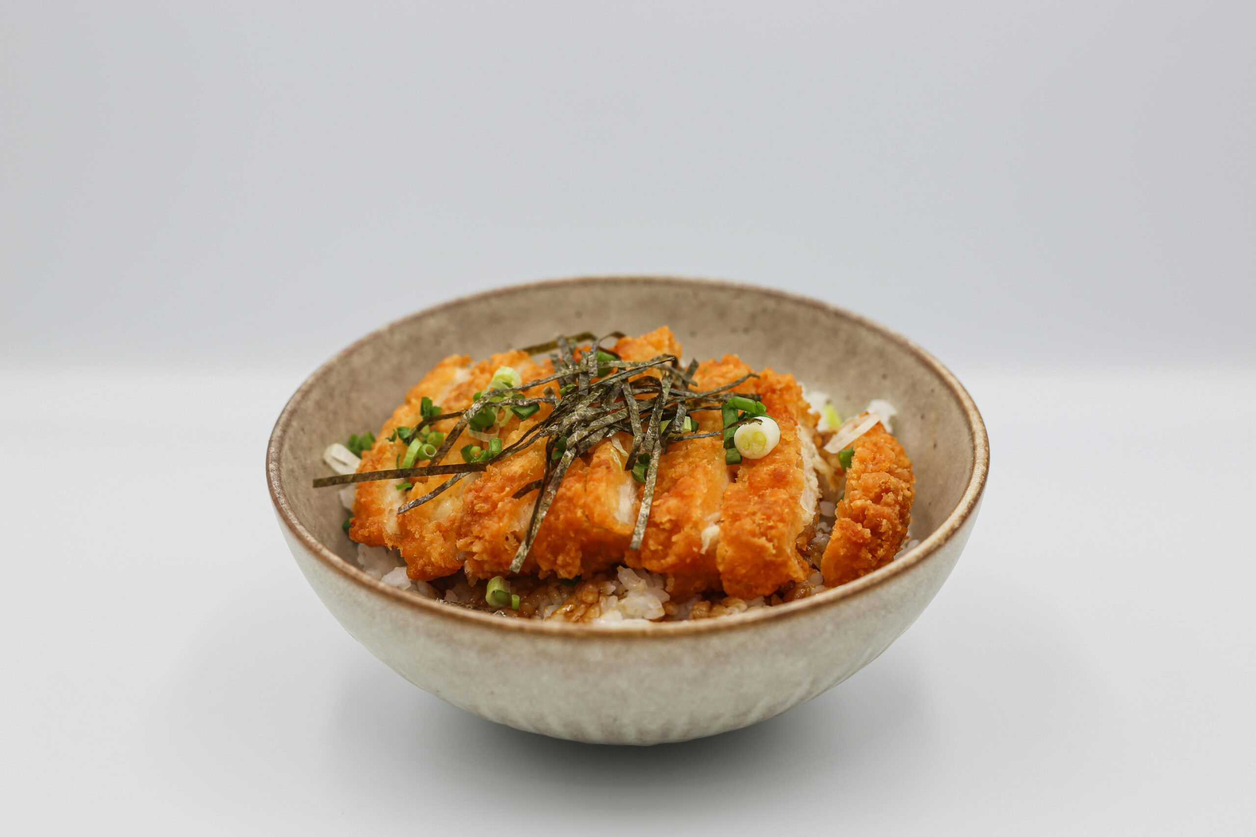 A mouthwatering chicken katsu served on steamed rice with savory toppings in a bowl.